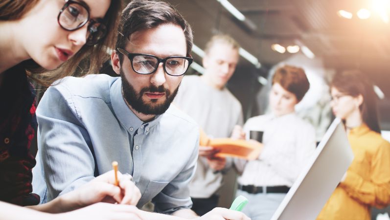 Menschen schauen gemeinsam auf den Bildschirm eines Laptops und besprechen etwas.