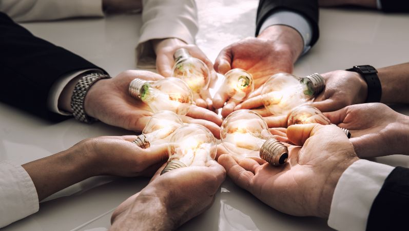 Symbolbild Austausch von Ideen: acht Hände halten leuchtende Glühbirnen in ihren Handflächen