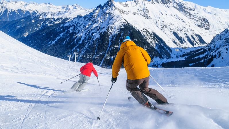 Skifahrer fahren eine verschneite Berglandschaft entlang.