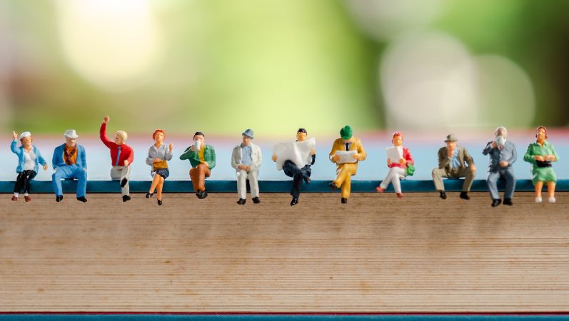 Symbolfoto: Zwölf verschiedene Miniaturfiguren sitzen auf einer Buchkante.
